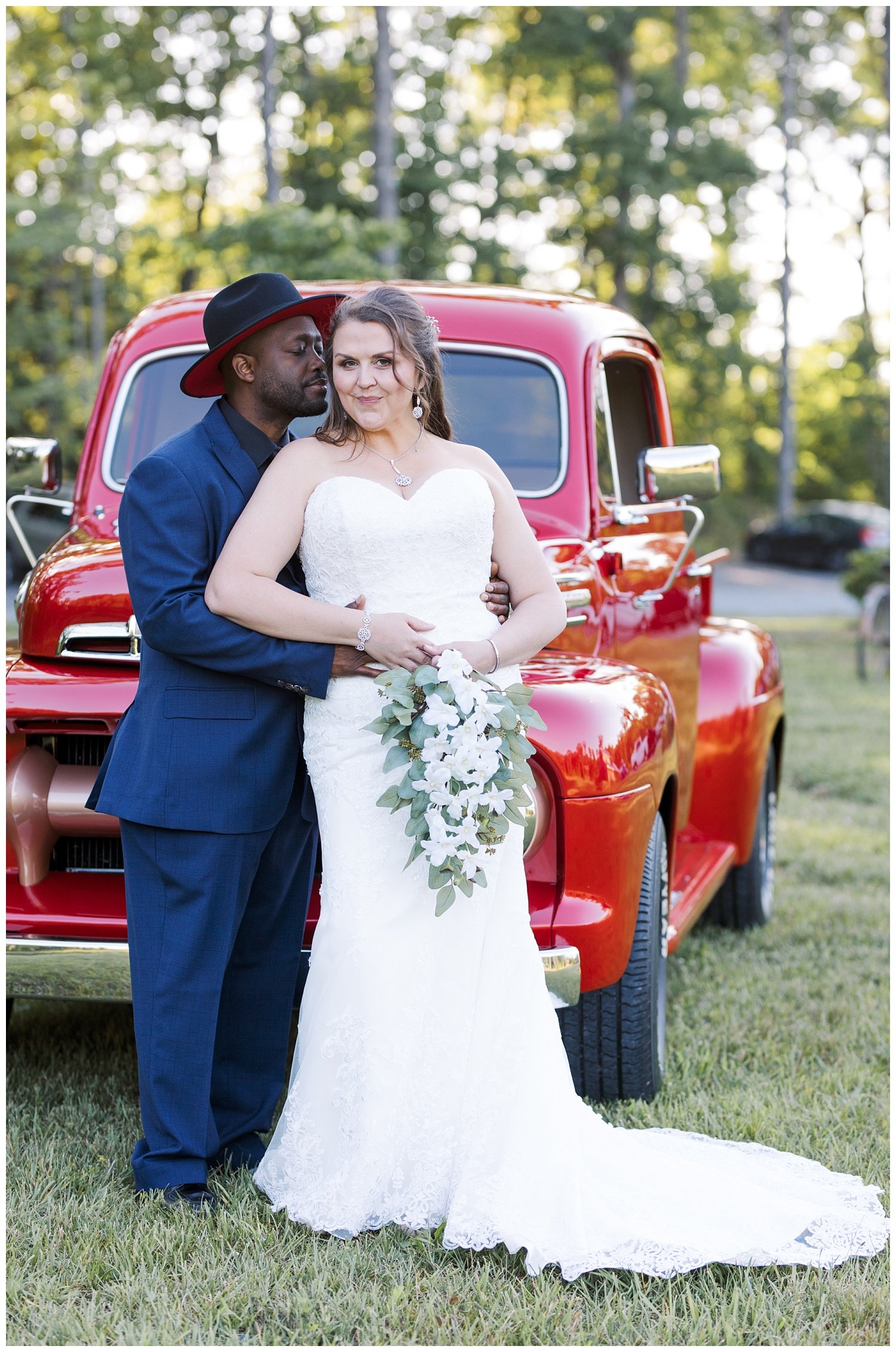 bride and groom posing in front of red truck at wedding