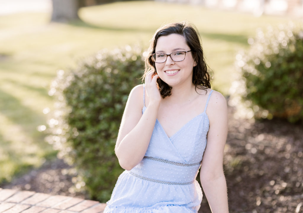 college senior wearing a light blue dress sitting on a brick bench