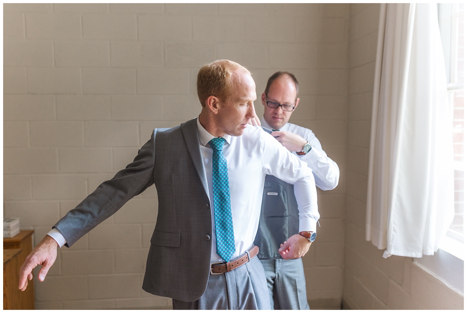 groomsmen helping groom put on his jacket while getting ready