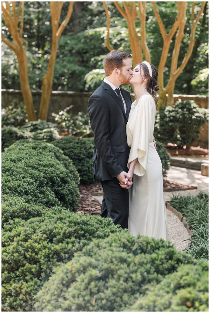 wedding couple kissing next to the bushes at the Swan House
