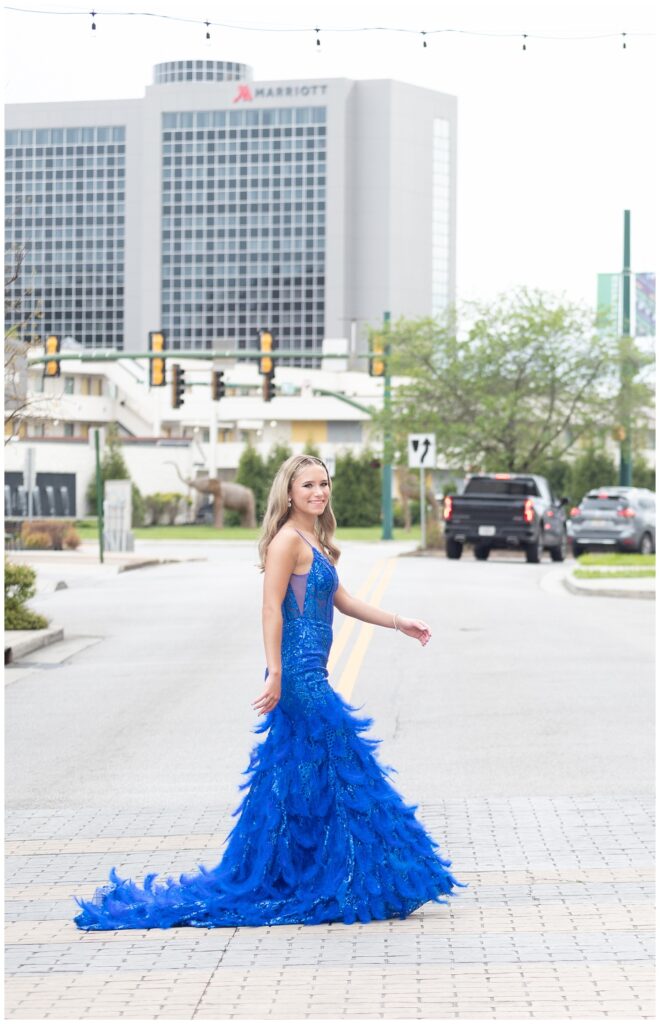 senior girl wearing a blue dress crossing the street for prom photos