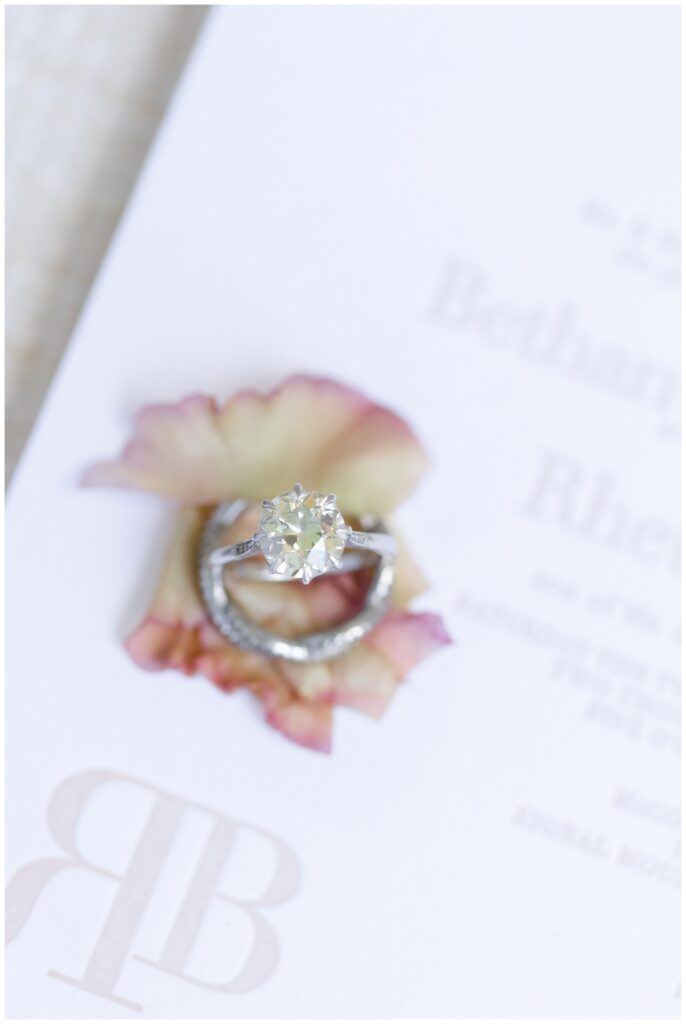 wedding rings sitting on top of flower petals and invitation