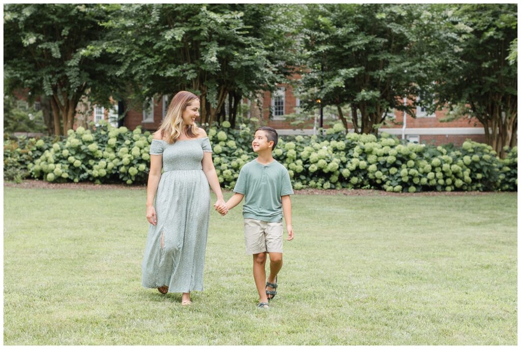 mom holding hands with her son and walking in the grass