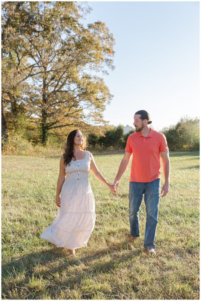 husband and wife walking together and holding hands in a field 