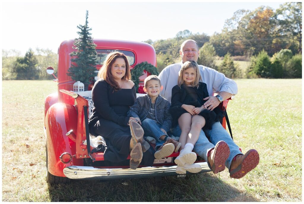 family sitting in the back of a classic red truck for holiday mini session