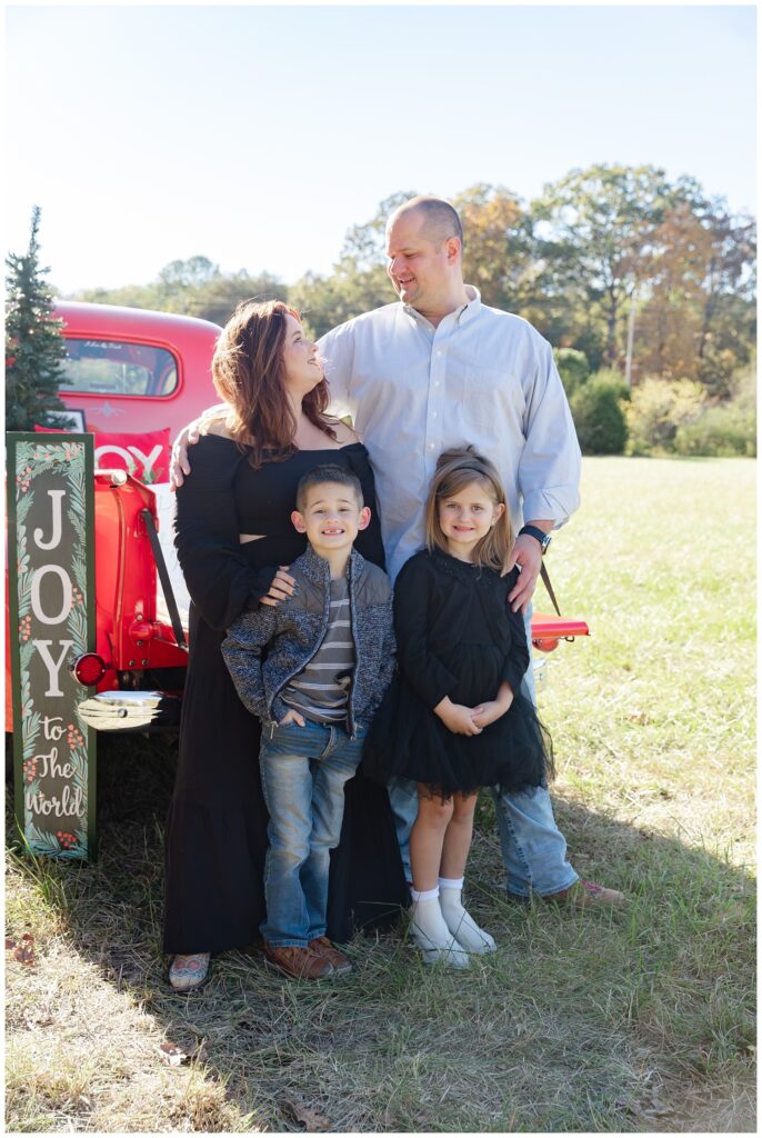 family standing in front of a red truck and joy sign for Christmas