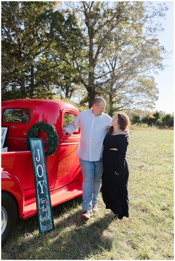 couple standing next to a red truck and a wreath for holiday mini session