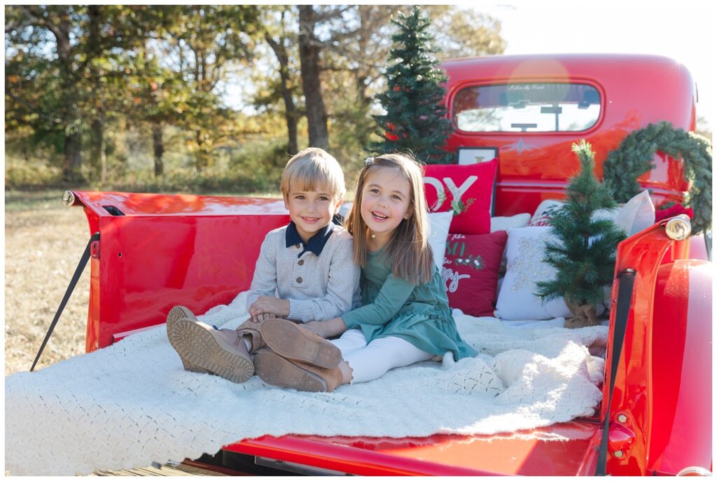 two kids laughing and smiling in the back of a classic red truck 