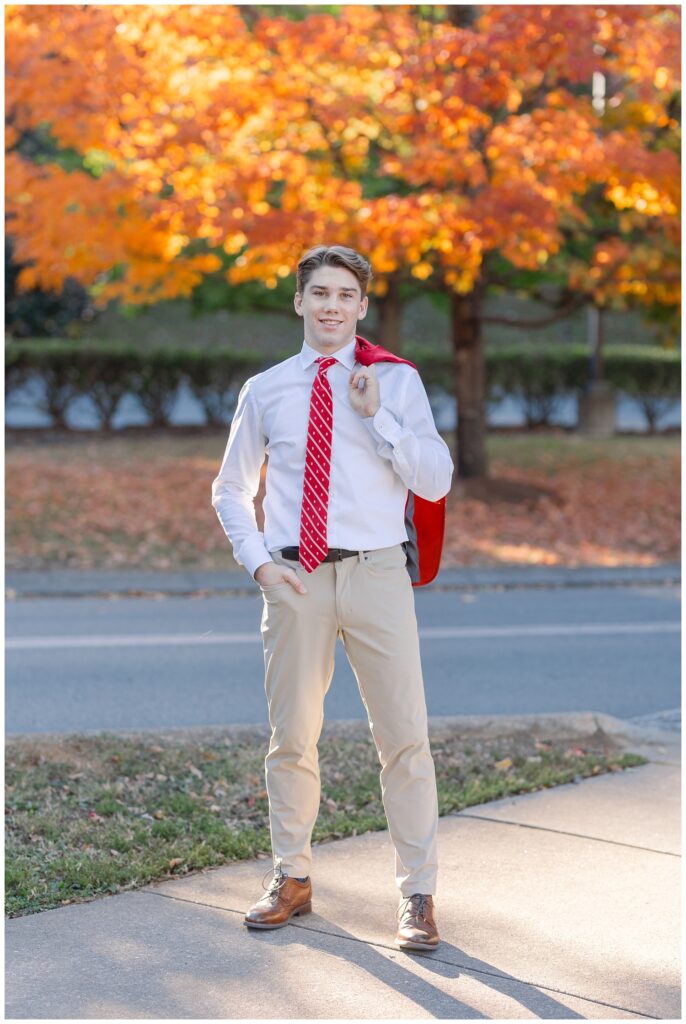 senior guy holding his red jacket over his shoulder in front of a orange tree