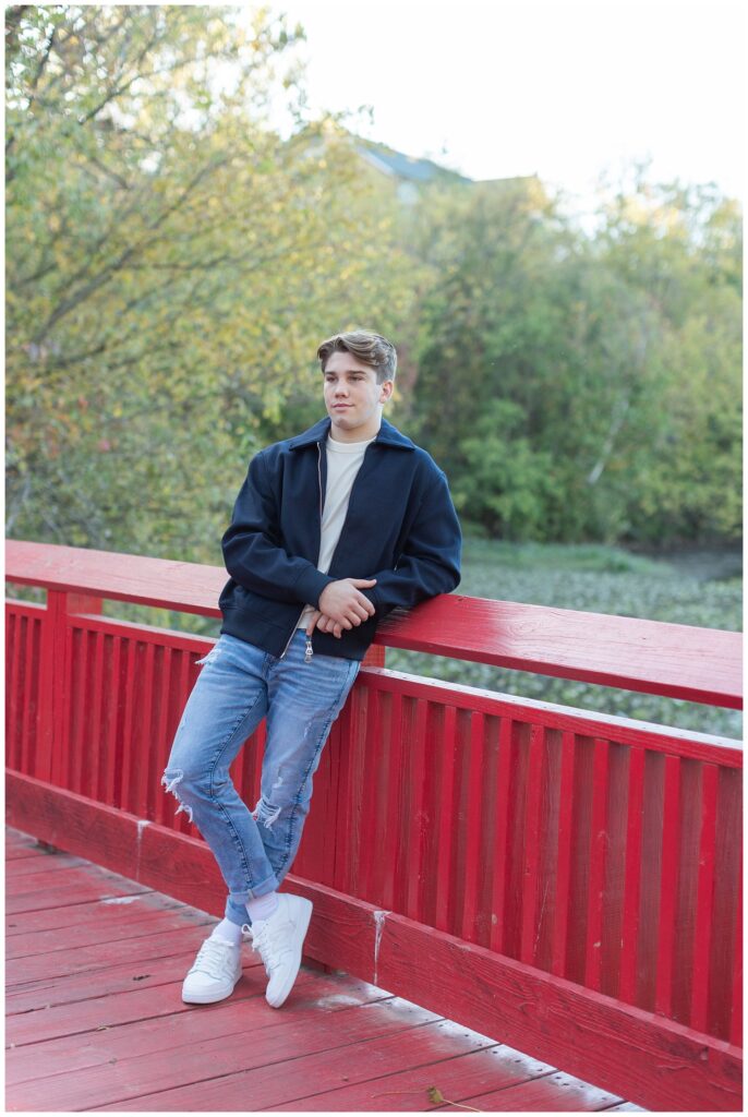 boy leaning against a red bridge for fall senior session