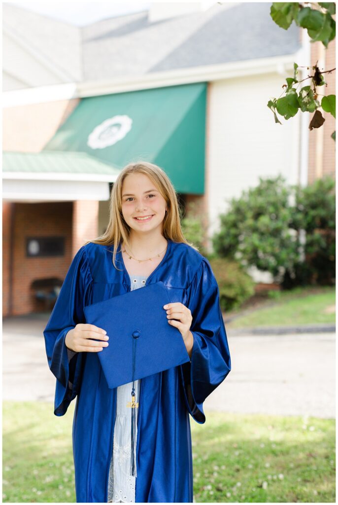 girl holding her blue cap and smiling under a tree