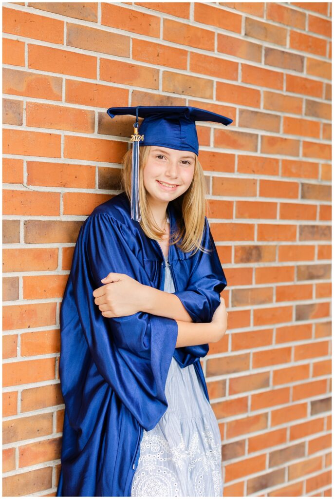 girl leaning against a brick wall wearing a blue cap and gown