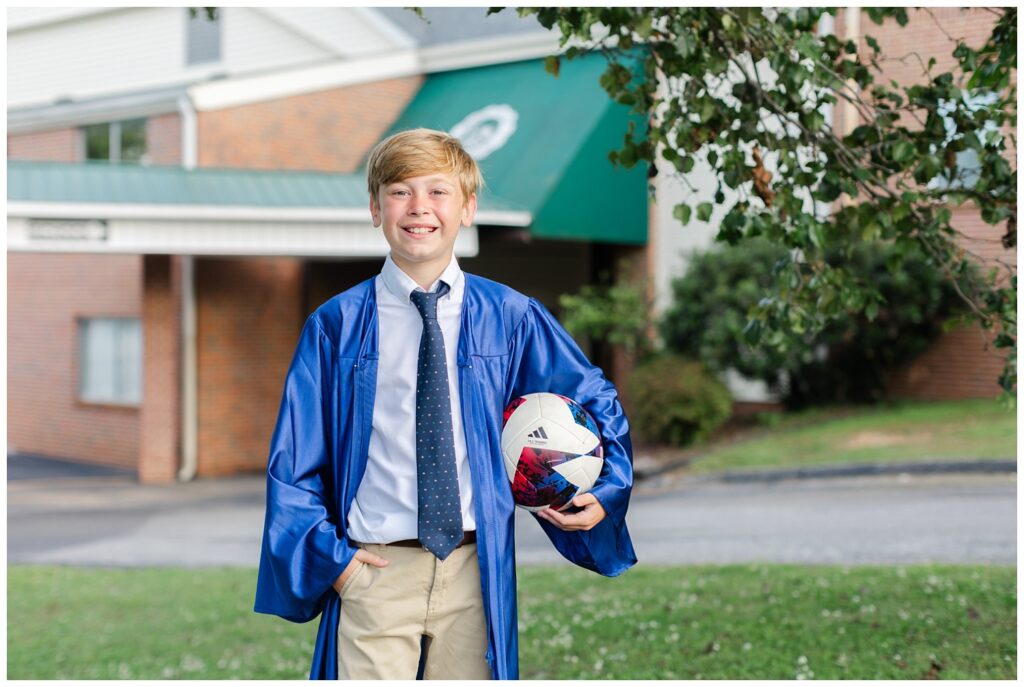 boy holding a soccer ball and wearing a blue cap and gown at mini session