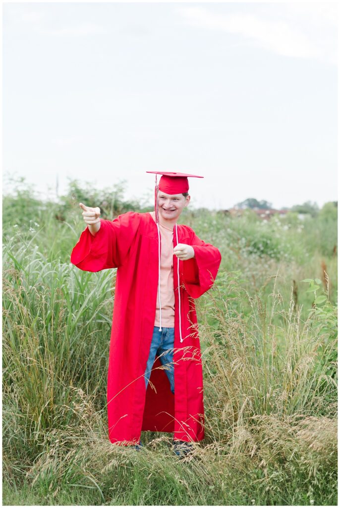 senior boy wearing his red graduation cap and gown at Sculpture Fields