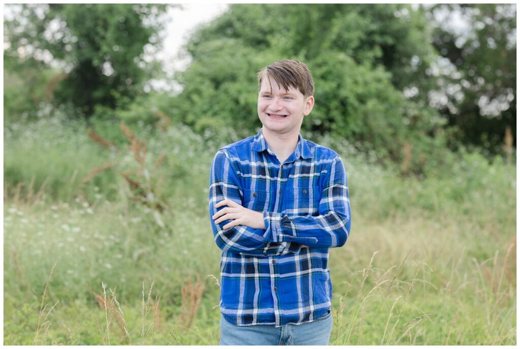 boy crossing his arms wearing a blue and white striped shirt in a field