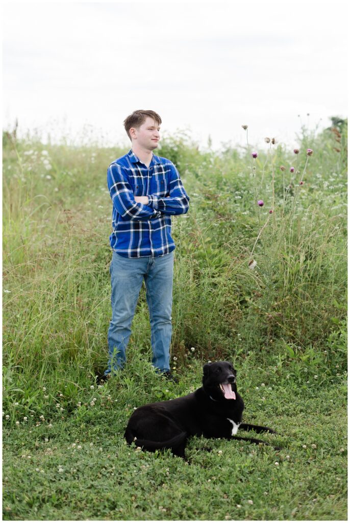 senior boy posing with his black dog in the grass at the Sculpture Fields