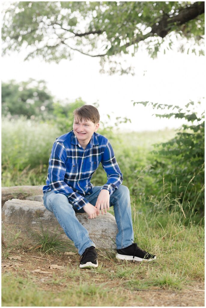 senior boy posing on a rock for portrait session at Sculpture Fields