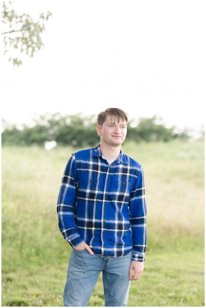 senior boy posing with his hand in his pocket wearing a white and blue striped shirt