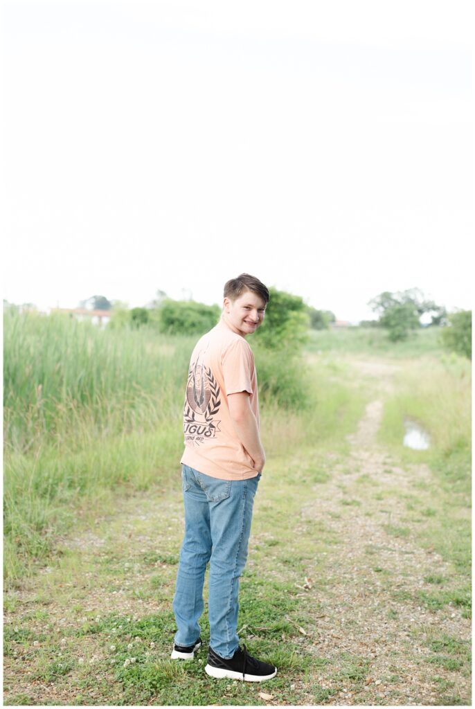 senior boy showing off the back of his shirt while posing on a trail