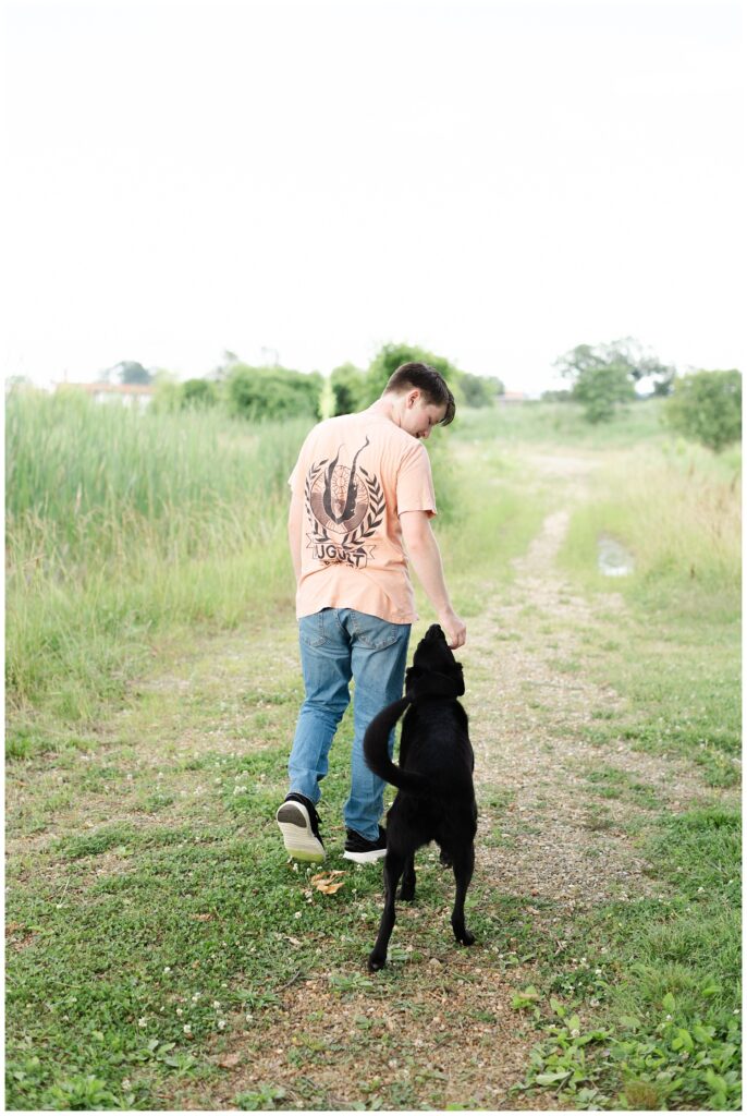 senior boy walking with his black dog on a trail at the Sculpture Fields