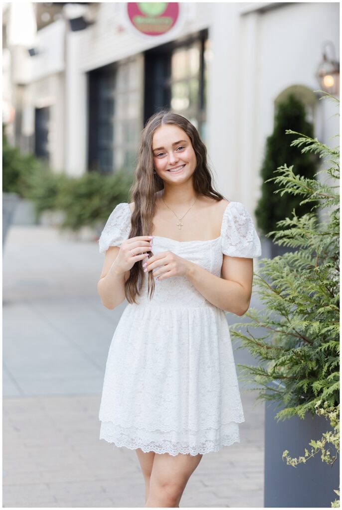 senior girl playing with her hair next to a large plant on a sidewalk