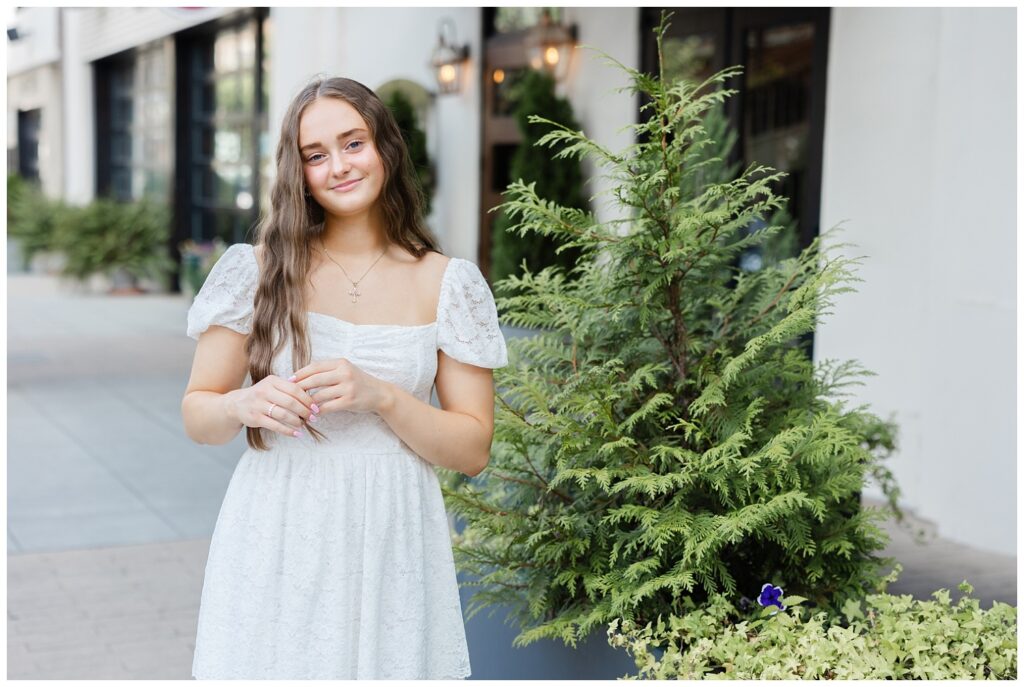 senior girl playing with her hair next to a large plant on a sidewalk