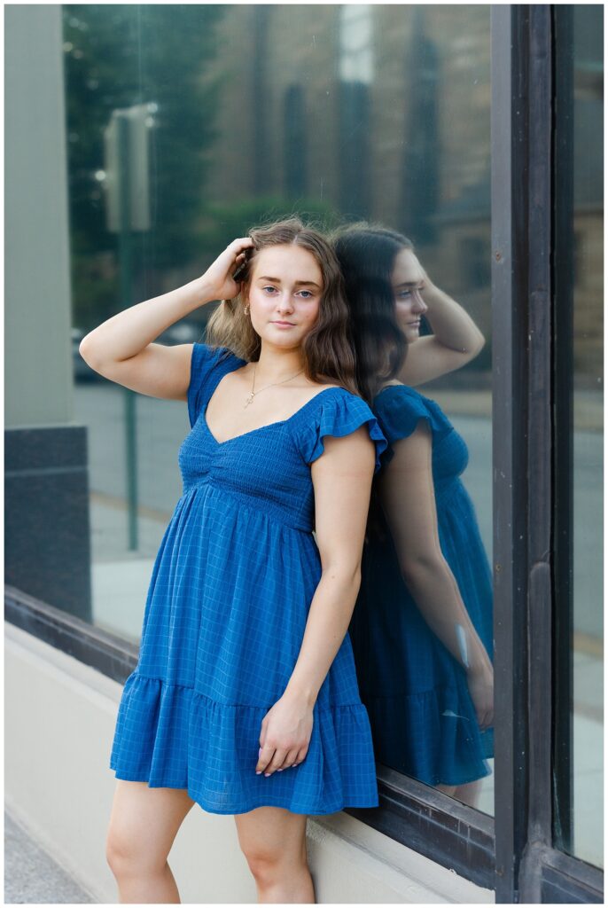 high school senior leaning against a large window with her reflection behind her 