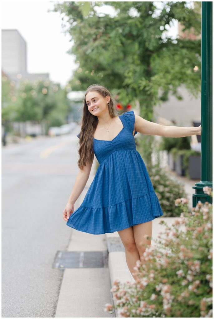 high school senior holding onto a green lamp post and hanging off while holding her dress 