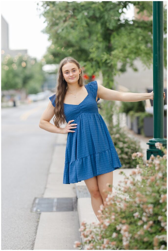 high school senior holding onto a green lamp post and hanging off with her hand on he waist