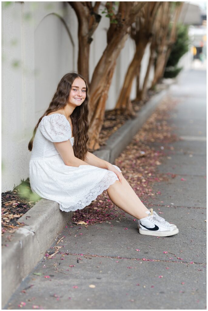 senior girl sitting on the curb along the sidewalk in downtown Chattanooga