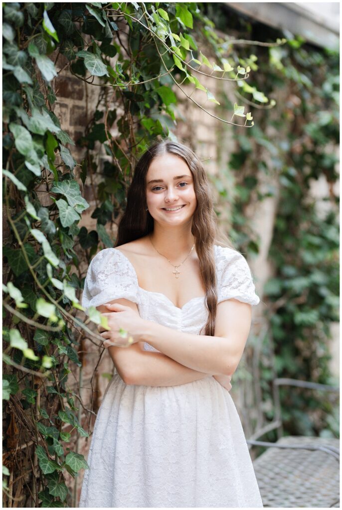 high school senior crossing her arms while posing next to a wall covered in ivy