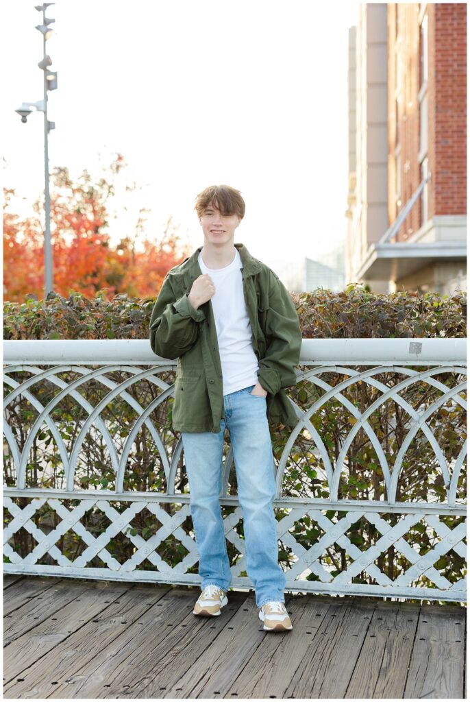 senior boy wearing jeans a dark green jacket while standing on the Walnut Street Bridge