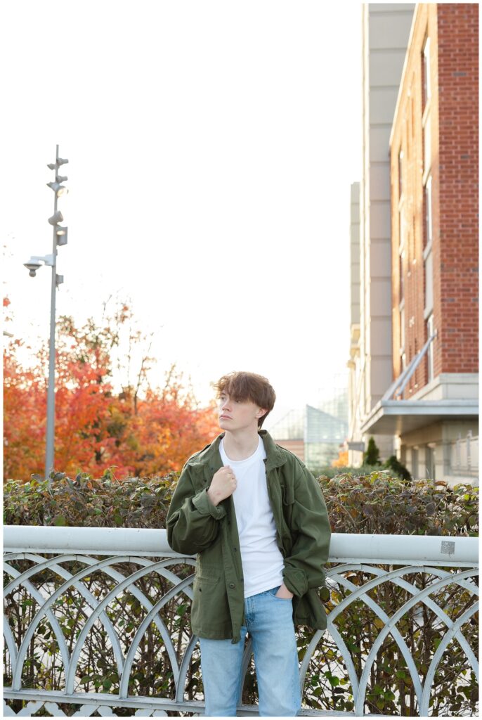 senior boy wearing jeans a dark green jacket while standing on the Walnut Street Bridge