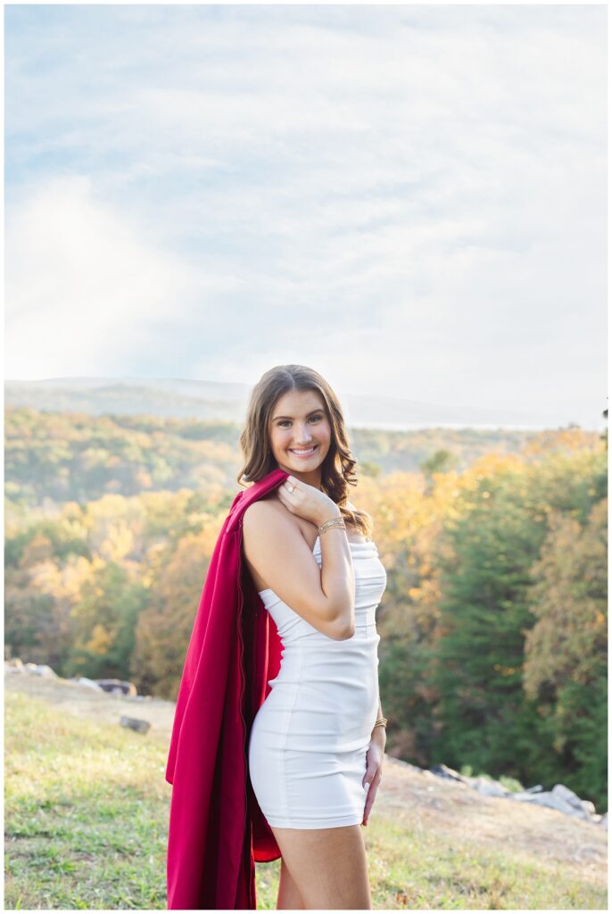 senior holding her red gown over her shoulder with mountains in the background