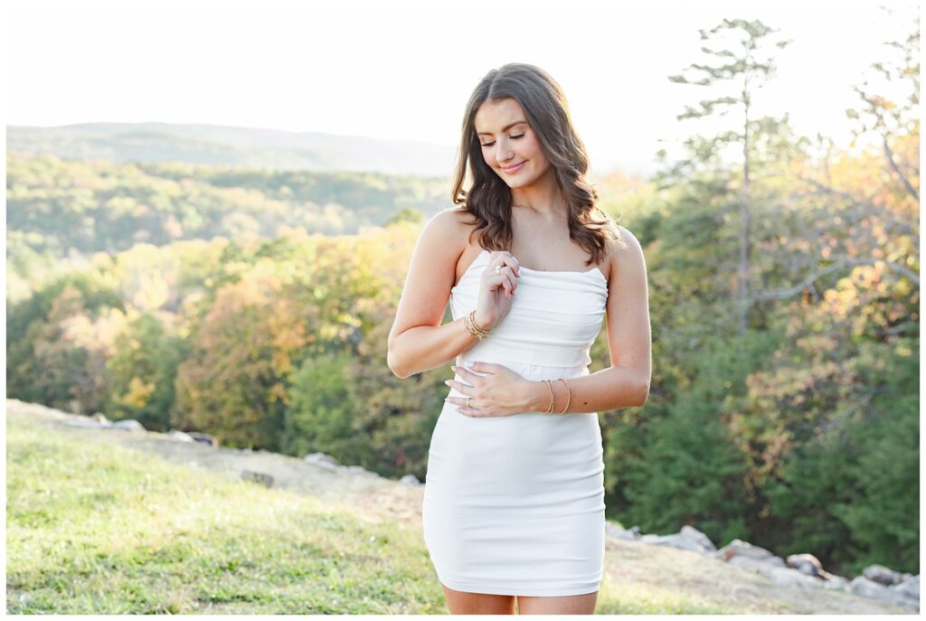 high school senior holding her hair and wearing a white dress looking down at her shoulder