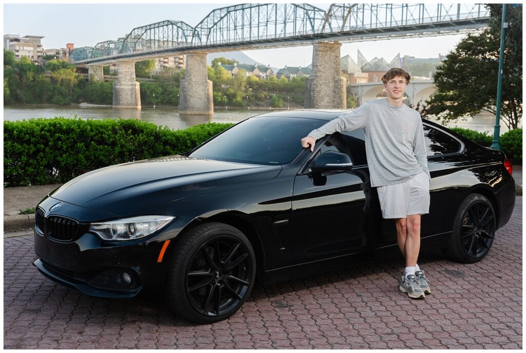 senior boy posing against his black two door BMW in Renaissance Park near the Walnut Street Bridge