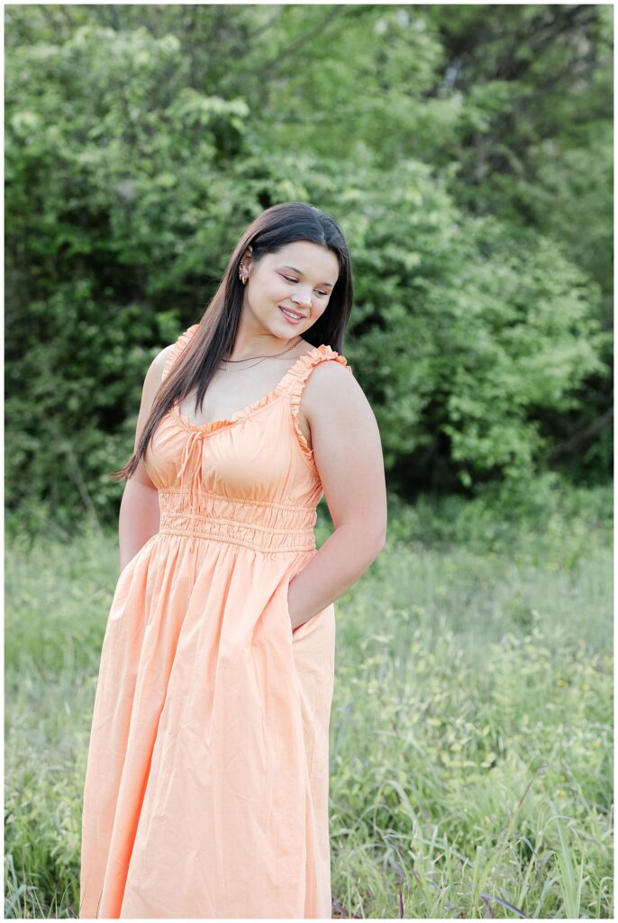 senior girl wearing an orange dress and posing in a field near Renaissance Park