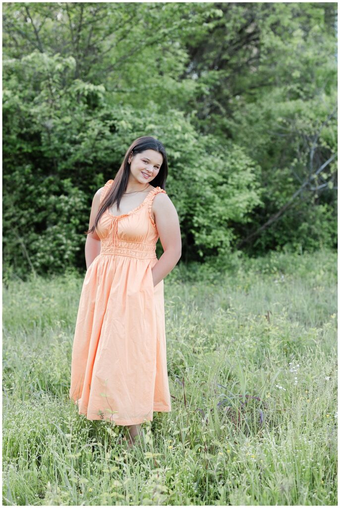 senior girl wearing an orange dress and posing in a field near Renaissance Park