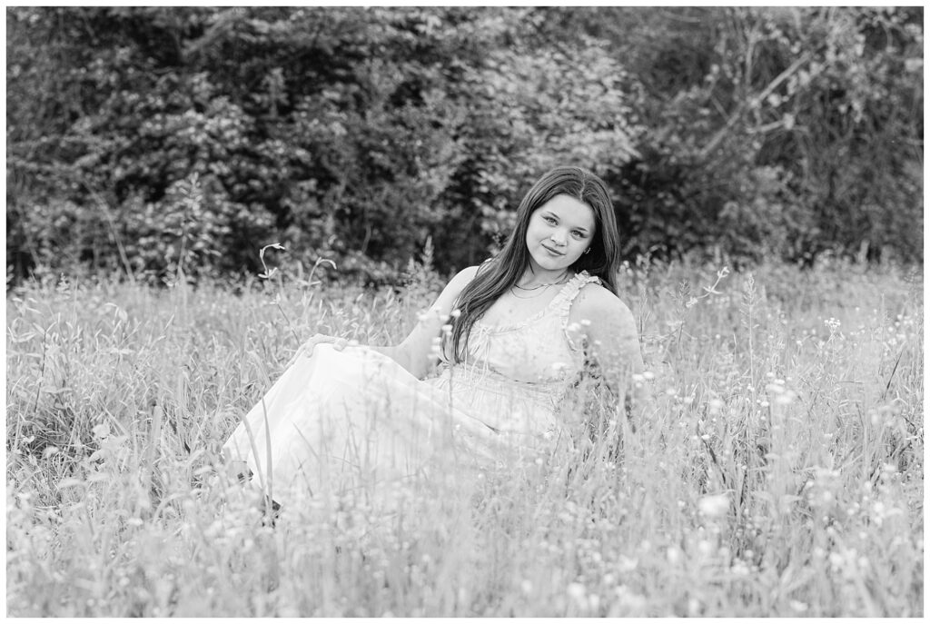 senior girl wearing an orange dress and sitting in a grassy field near Renaissance Park