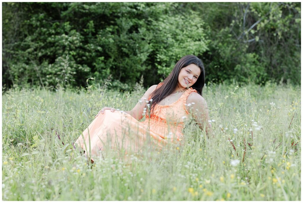 senior girl sitting in a grassy field in Renaissance Park