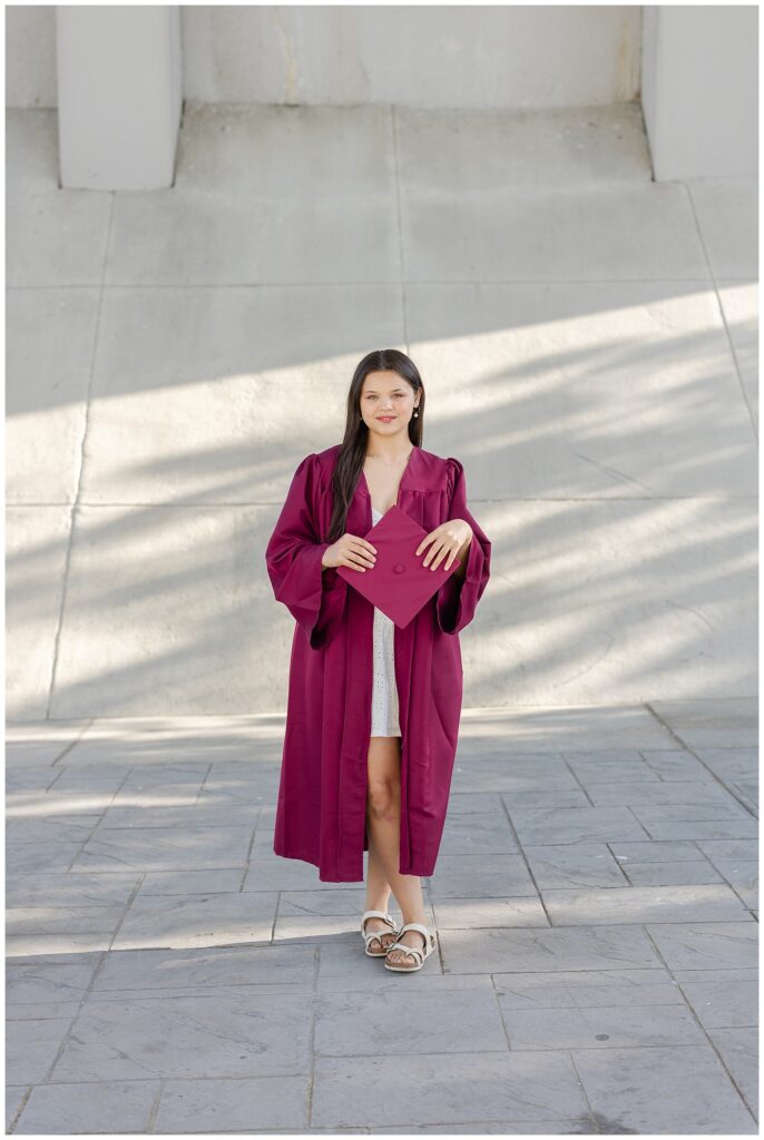 high school senior wearing a maroon cap and gown under the Market Street Bridge