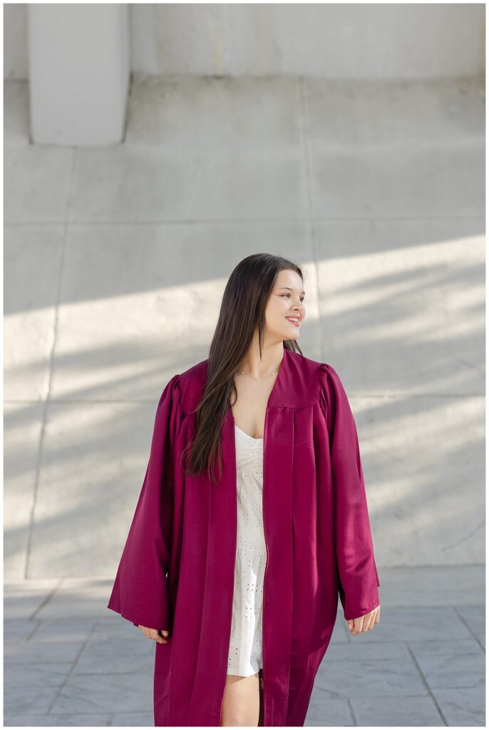 girl wearing a maroon graduation gown and looking off for senior photoshoot