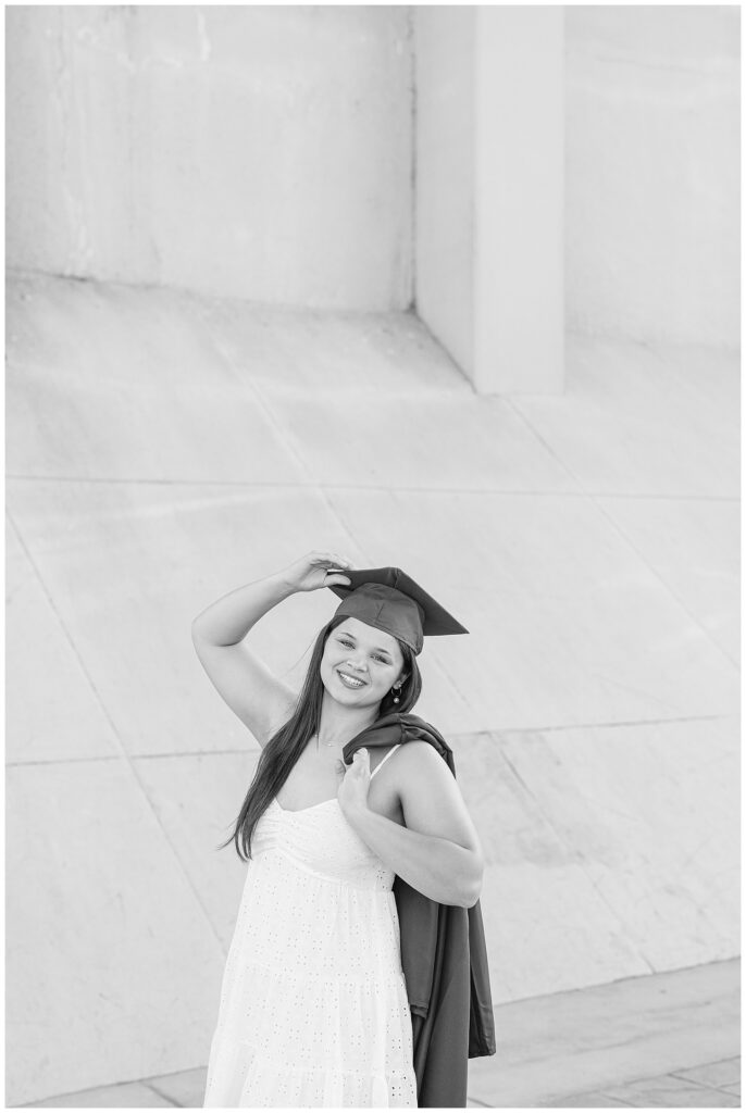 senior girl holding onto her cap while holding her graduation gown over her shoulder