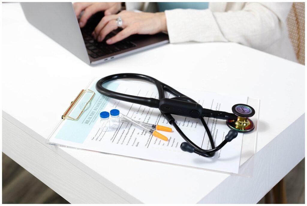 stethoscope sitting on a clipboard and intake form with vials of medicine on corner of white desk