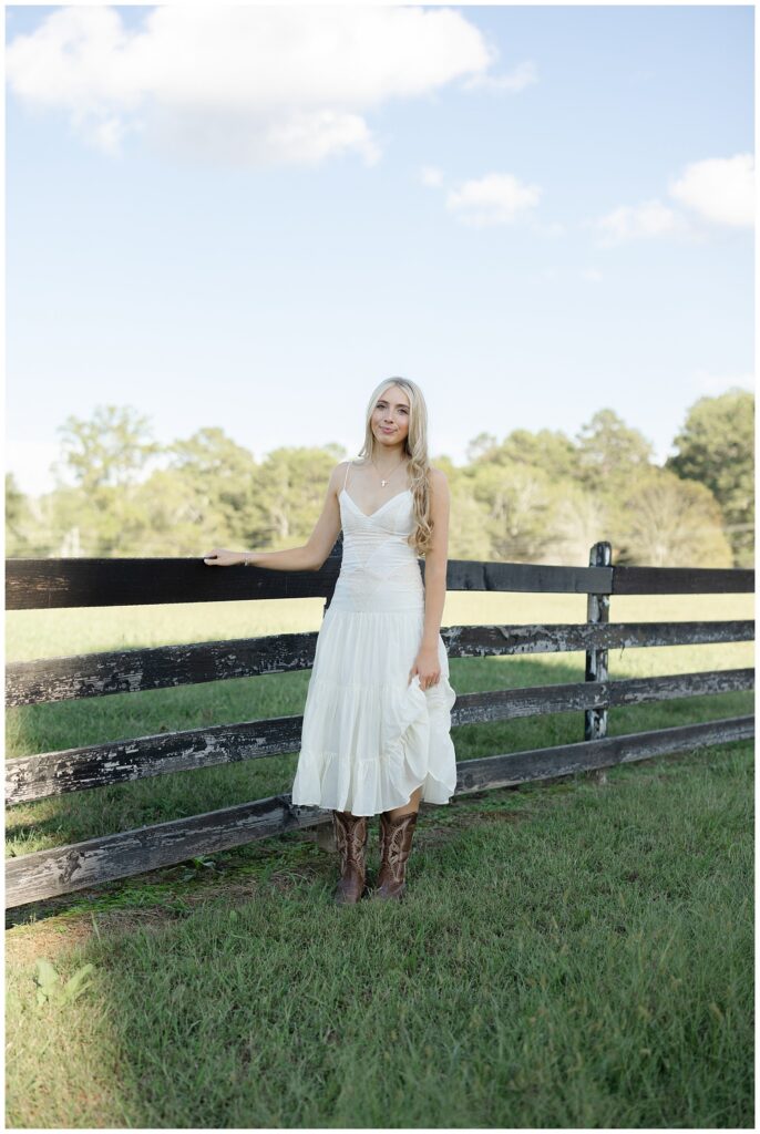 high school senior leaning against a fence on her family farm in north Georgia wearing a white dress