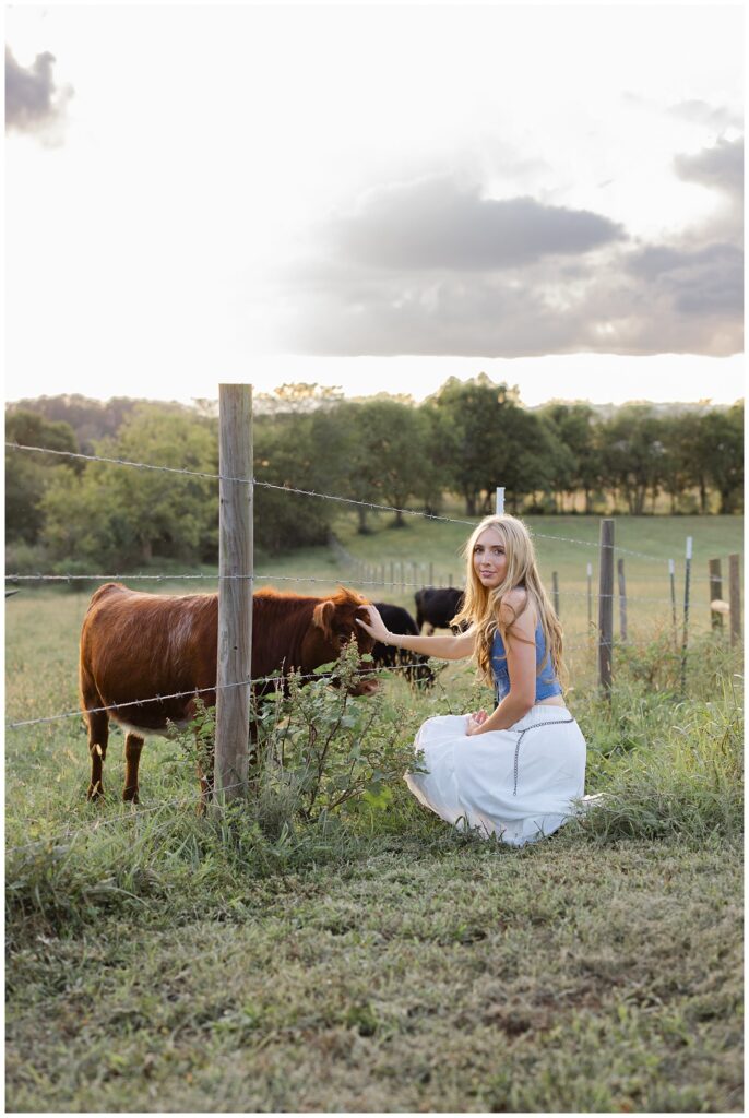 high school senior girl bending down to pet cows on her family farm near Chattanooga