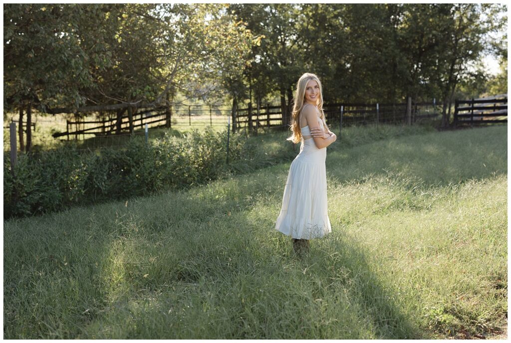 high school senior wearing a white dress and cowboy boots standing in a tall field in Chattanooga