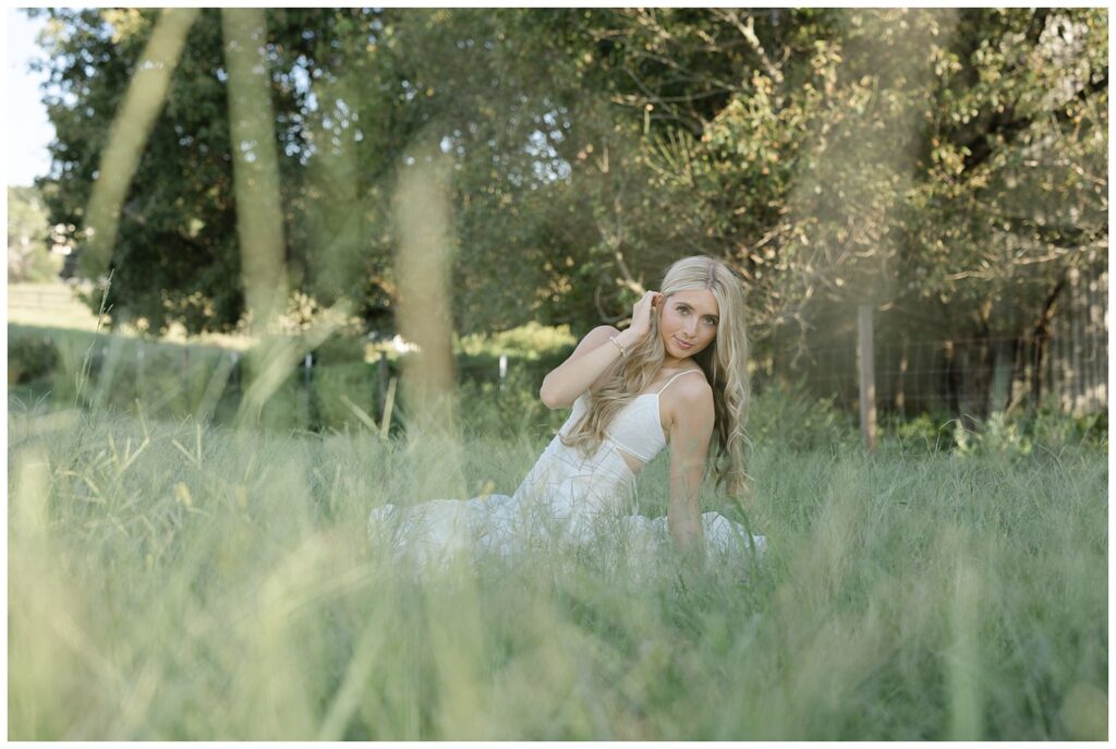 senior leaning back and sitting in the grass of her family farm in north Georgia