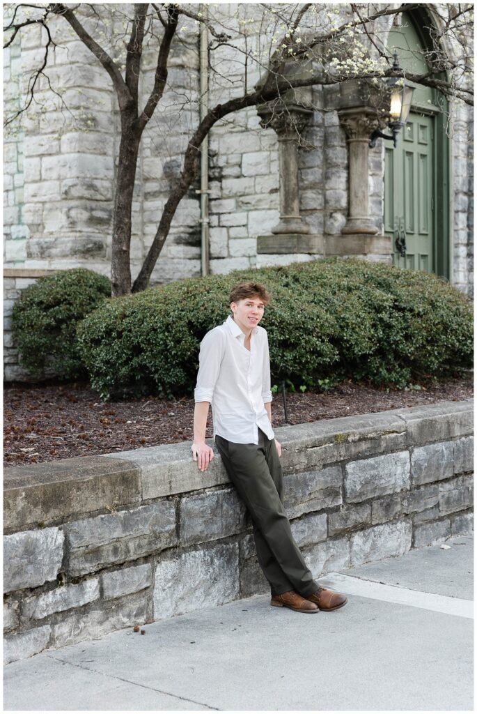 senior guy leaning against a stone wall next to an old church tower at Phillips Park in Chattanooga