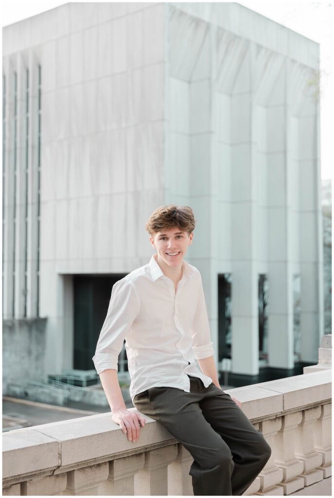 high school senior guy sitting on the edge of the courthouse balcony with Chattanooga buildings in the background
